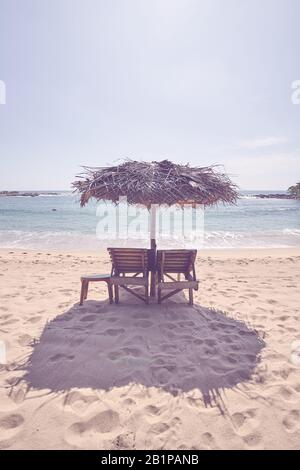 Lettini in legno sotto l'ombrello di palma su una spiaggia tropicale, tonificante colore applicato. Foto Stock