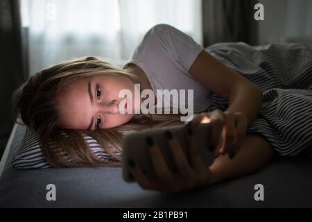 Bella, giovane donna che dorme nel suo letto con il suo cellulare vicino a lei. Smartphone in Bed Mobile / smartphone Addiction Concetto. Foto Stock