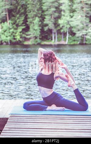 Bella ragazza in una posa yoga sul lago. Eka Pada Rajakapotasana . Una Posa Di Piccione Del Re Del Leged. Il concetto di pacificazione, stile di vita sano. Foto Stock