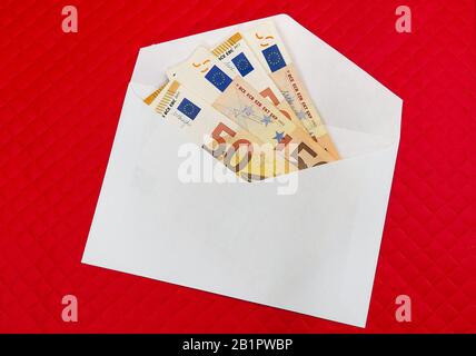 Banconote in euro in busta bianca su sfondo rosso. Concetto di tangente, dale, regalo, trasferimento di denaro Foto Stock