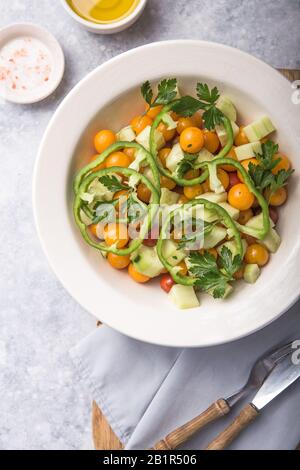 Insalata con cetrioli, pomodori ciliegi, pomergranate, cipolla e paprika. Vista dall'alto su sfondo grigio in cemento. Foto Stock