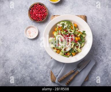 Insalata con cetrioli, pomodori ciliegi, pomergranate, cipolla e paprika. Vista dall'alto su sfondo grigio in cemento. Foto Stock