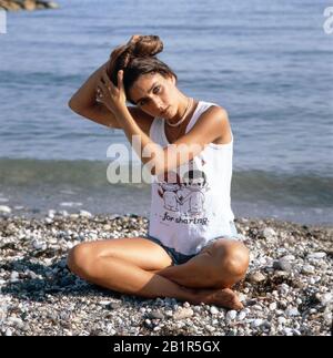 Homerory der italienisch amerikanischen Sängerin und Schauspielerin Romina Power im Schneidersitz am Strand, Italien mitte 1980er Jahre. Home storia della cantante e attrice italo-americana Romina Power seduto a gambe incrociate sulla spiaggia, Italia a metà 1980s. Foto Stock