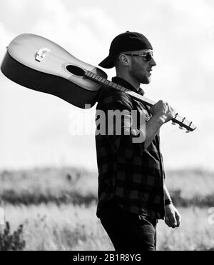 Trasognata wanderer. Atmosfera pacifica. Escursionismo canzone. Un musicista in cerca di ispirazione. Uniti con la natura. Ispirando la natura. Uomo bello con la chitarra a contemplare la natura. In cerca di muse. La vacanza estiva. Foto Stock