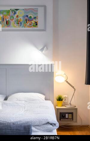 Budapest, Ungheria - 10 novembre 2019: Dettaglio di elegante camera da letto minimalista con testiera grigia, immagine colorata e cassaforte comodino Foto Stock