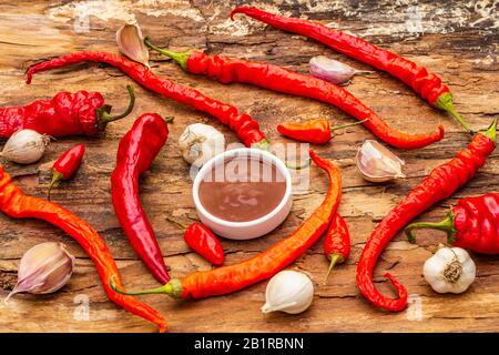 Salsa tradizionale Thai Sriracha con ingredienti. Peperoncino rosso e arancio leggermente secco, aglio. In ciotola di ceramica, sfondo di corteccia di legno Foto Stock