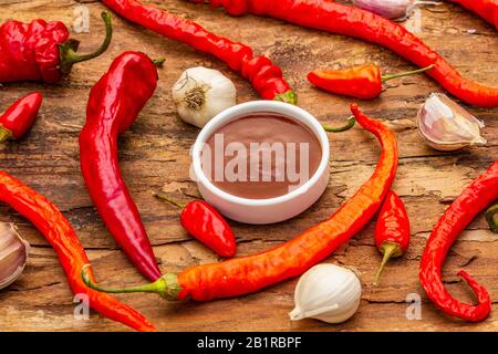 Salsa tradizionale Thai Sriracha con ingredienti. Peperoncino rosso e arancio leggermente secco, aglio. In ciotola di ceramica, sfondo di corteccia di legno, primo piano Foto Stock