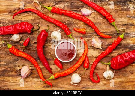 Salsa tradizionale Thai Sriracha con ingredienti. Peperoncino rosso e arancio leggermente secco, aglio. In vaso di ceramica, sfondo di corteccia di legno, vista dall'alto Foto Stock