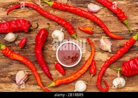 Salsa tradizionale Thai Sriracha con ingredienti. Peperoncino rosso e arancio leggermente secco, aglio. In vaso di ceramica, sfondo di corteccia di legno, vista dall'alto Foto Stock