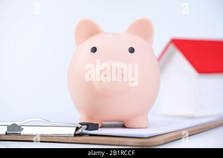 Banca piggy, modello di casa di legno bello sopra un contratto firmato su sfondo bianco, concetto di risparmio di soldi per comprare un'assicurazione domestica, primo piano, copia s. Foto Stock