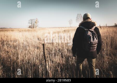 Viaggiatore maschile con uno zaino che cammina verso l'orizzonte su un prato selvaggio Foto Stock