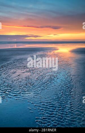 Spettacolare tramonto costiero sulla sabbia modellata, orizzonte cielo atmosferico, spiaggia, vita costiera, romantico, sera, cielo drammatico e luminoso, costa Foto Stock