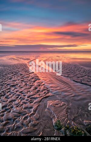 Spettacolare tramonto costiero sulla sabbia modellata, orizzonte cielo atmosferico, spiaggia, vita costiera, romantico, sera, cielo drammatico e luminoso, costa Foto Stock