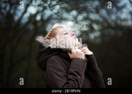 Donna con occhi chiusi che si strappa nella giacca invernale, Foto Stock