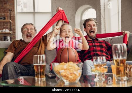 Vittoria. La famiglia è entusiasta e felice di guardare la partita di basket, campionato sul divano a casa. Fan emozionali che acclamano per la squadra nazionale preferita. Figlia, papà e nonno. Sport, TV, divertirsi. Foto Stock