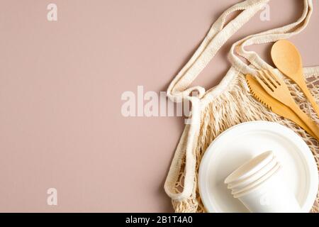 Borsa per alimentari eco-friendly in mesh con set di posate in legno, tazza di carta e piastra. Disposizione piatta, vista dall'alto. Zero rifiuti, tassa plastica concetto. Stile di vita sostenibile Foto Stock