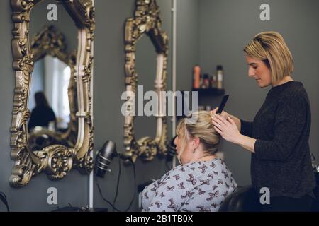Un parrucchiere che mette in piega i capelli di una donna di mezza età in un parrucchiere o in un parrucchiere Foto Stock