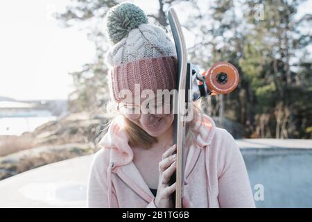 ritratto di una donna che guarda giù tenendo il suo skateboard in uno skatepark Foto Stock