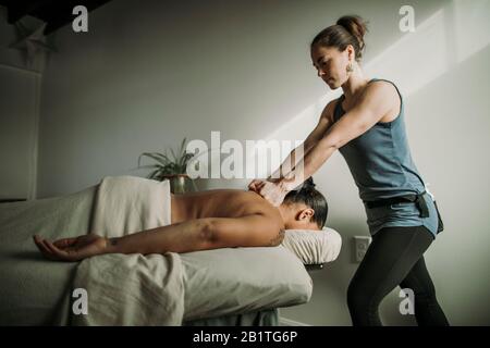 Massaggio femminile terapista massaggi le spalle del paziente afroamericano Foto Stock