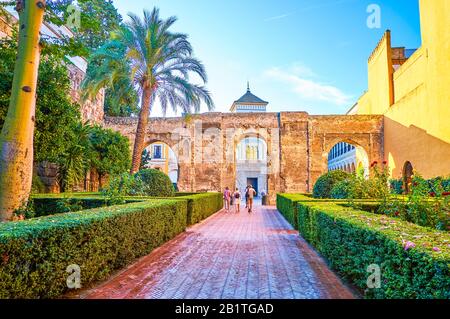 Siviglia, SPAGNA - 1 OTTOBRE 2019: Il lungo vicolo tra il verde conduce agli antichi resti di Almohad muro con archi e il grande patio de la Mon Foto Stock