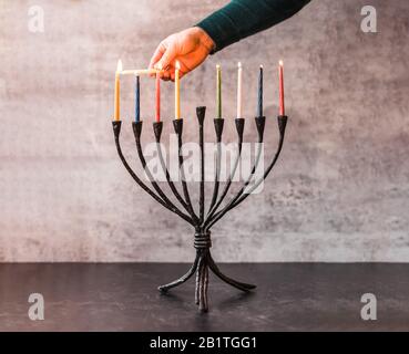 Immagine ritagliata di una mano che illumina candele su menorah per Hanukkah. Foto Stock