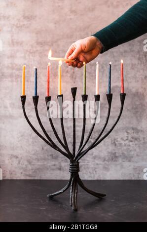 Immagine ritagliata di una mano che illumina candele su menorah per Hanukkah. Foto Stock