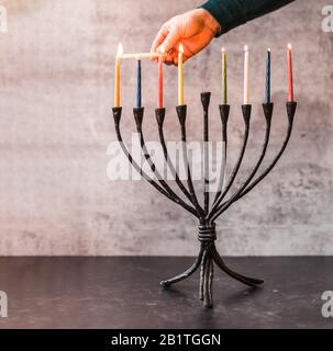 Immagine ritagliata di una mano che illumina candele su menorah per Hanukkah. Foto Stock