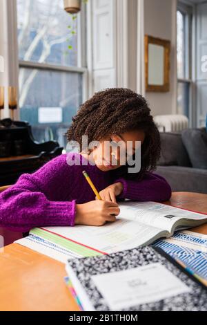 La ragazza fa i compiti mentre si siede al tavolo nel soggiorno Foto Stock