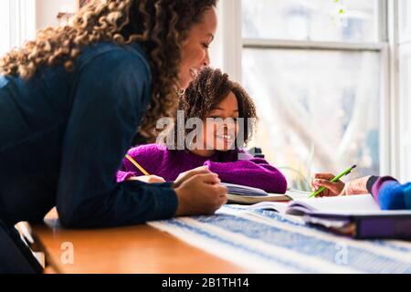 Madre sorridente che assiste le figlie nel fare i compiti a casa Foto Stock