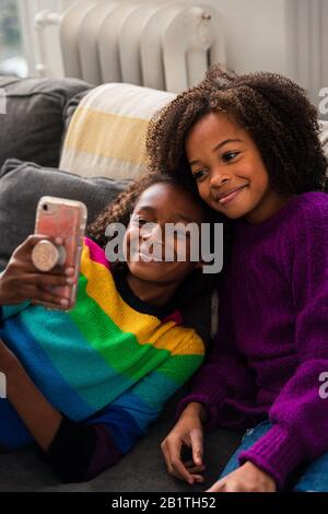 Sorride le sorelle che prendono selfie mentre si appoggia sul divano nel soggiorno a casa Foto Stock