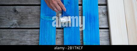 Vista dall'alto di tavole di legno per verniciatura a mano femmina con vernice blu utilizzando una spazzola. Immagine a vista larga. Foto Stock