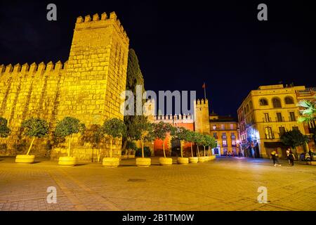 La vista notturna sulla Puerta del Leon medievale illuminata con torre alta e le mura del Palazzo Alcazar di Siviglia, Spagna Foto Stock