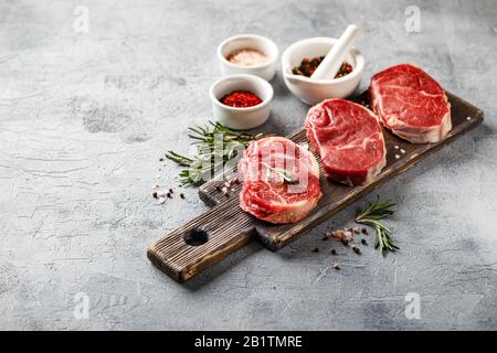 Tre pezzi di bistecca tradizionale sottile tagliata dal filetto su tagliere di legno con olio d'oliva, sale, rosmarino e pepe. Raw Black Angus Prim Foto Stock