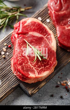 Tre pezzi di bistecca tradizionale sottile tagliata dal filetto su tagliere di legno con olio d'oliva, sale, rosmarino e pepe. Raw Black Angus Prim Foto Stock