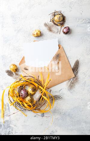 Uova di quaglia di Pasqua di colore giallo e viola con piume in piccoli nidi e carta di auguri in involucro. Profondità di campo bassa. Vista dall'alto. Spazio per te Foto Stock