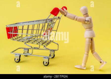 Uomo di legno che spinge un carrello sulla priorità bassa gialla. Vada per il concetto di shopping. Foto Stock