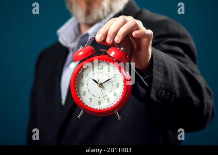 Uomo d'affari con bearded nel vestito che tiene la sveglia rossa. Concetto di gestione del tempo Foto Stock