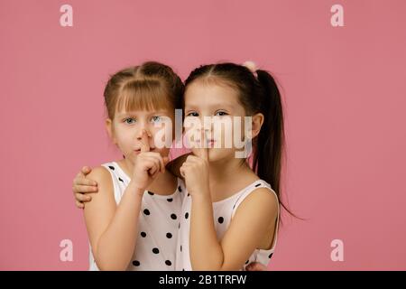 due belle ragazze piccole che chiedono di essere tranquille con il dito sulle labbra su sfondo rosa. bambini che mostrano segno shh Foto Stock