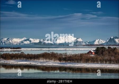 Snowscape in Norvegia con montagne, alberi, acqua e un fienile rosso. Foto Stock