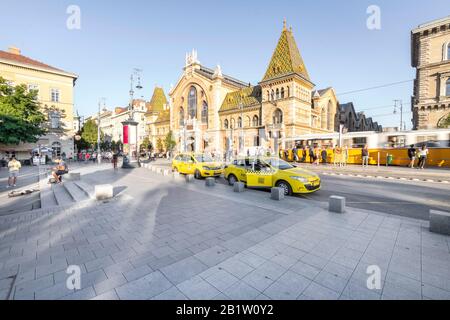 Budapest, Ungheria - 13 settembre 2019: La Grande Sala del mercato Vasarsarnok su piazza Fovam con persone che godono del sole e taxi in attesa di parcheggio. Foto Stock