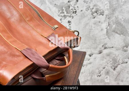 Borsa da lavoro in pelle e accessori nella sala da lavoro con parete in cemento grigio, tavolo in legno e sedia in pelle. Foto Stock