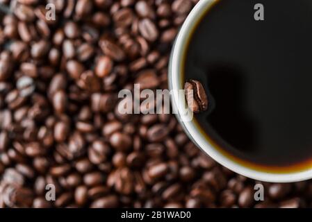 Un chicco di caffè galleggiante in una tazza di caffè nero. Foto Stock