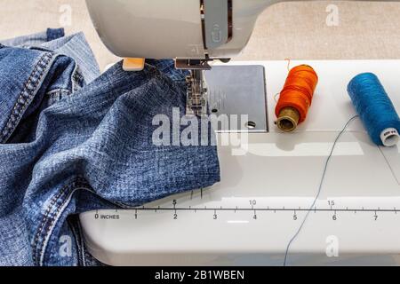 Piedino per macchina da cucire su denim. Forbici, rocchetti di filo. Si erge su un tavolo, con sfondo in legno Foto Stock