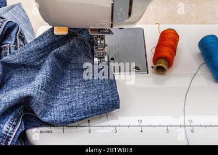 Piedino per macchina da cucire su denim. Forbici, rocchetti di filo. Si erge su un tavolo, con sfondo in legno Foto Stock