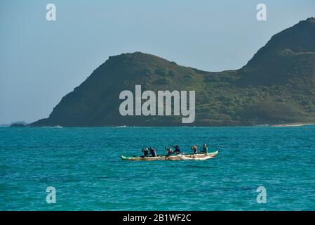 Persone che pagaiano in canoa outrigger in acque turchesi al largo di Lanikai Beach, l'isola di Moku Nui dietro (parte delle isole Mokulua), Oahu, Kailua, Hawaii, USA Foto Stock