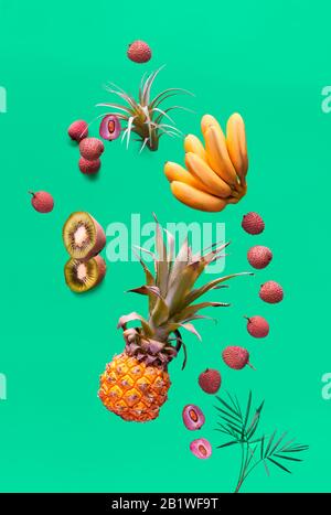 Assortimento di frutta tropicale e bottiglia di frullato arancione su sfondo verde. Ananas, kiwano, kiwi, lichee e banana - frutti esotici, levitazione a Foto Stock