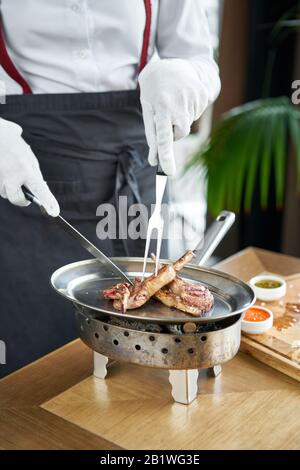 Il cameriere è macelleria con un coltello. Carré di agnello , grigliate di carne con osso. Ristorante Barbecue menu, una serie di foto di tipi diversi di carne Foto Stock