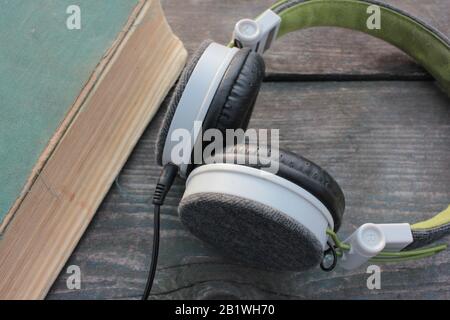 Vecchio libro shabby e cuffie su un tavolo di legno ruvido, all'aperto. Vista dall'alto Foto Stock