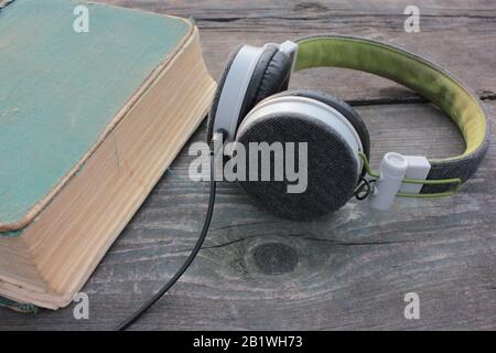 Vecchio libro shabby e cuffie su un tavolo di legno ruvido, all'aperto. Vista dall'alto Foto Stock