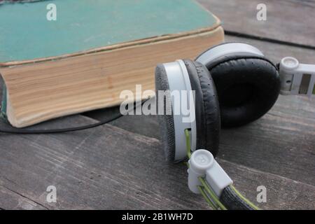 Vecchio libro shabby e cuffie su un tavolo di legno ruvido, all'aperto. Vista dall'alto Foto Stock